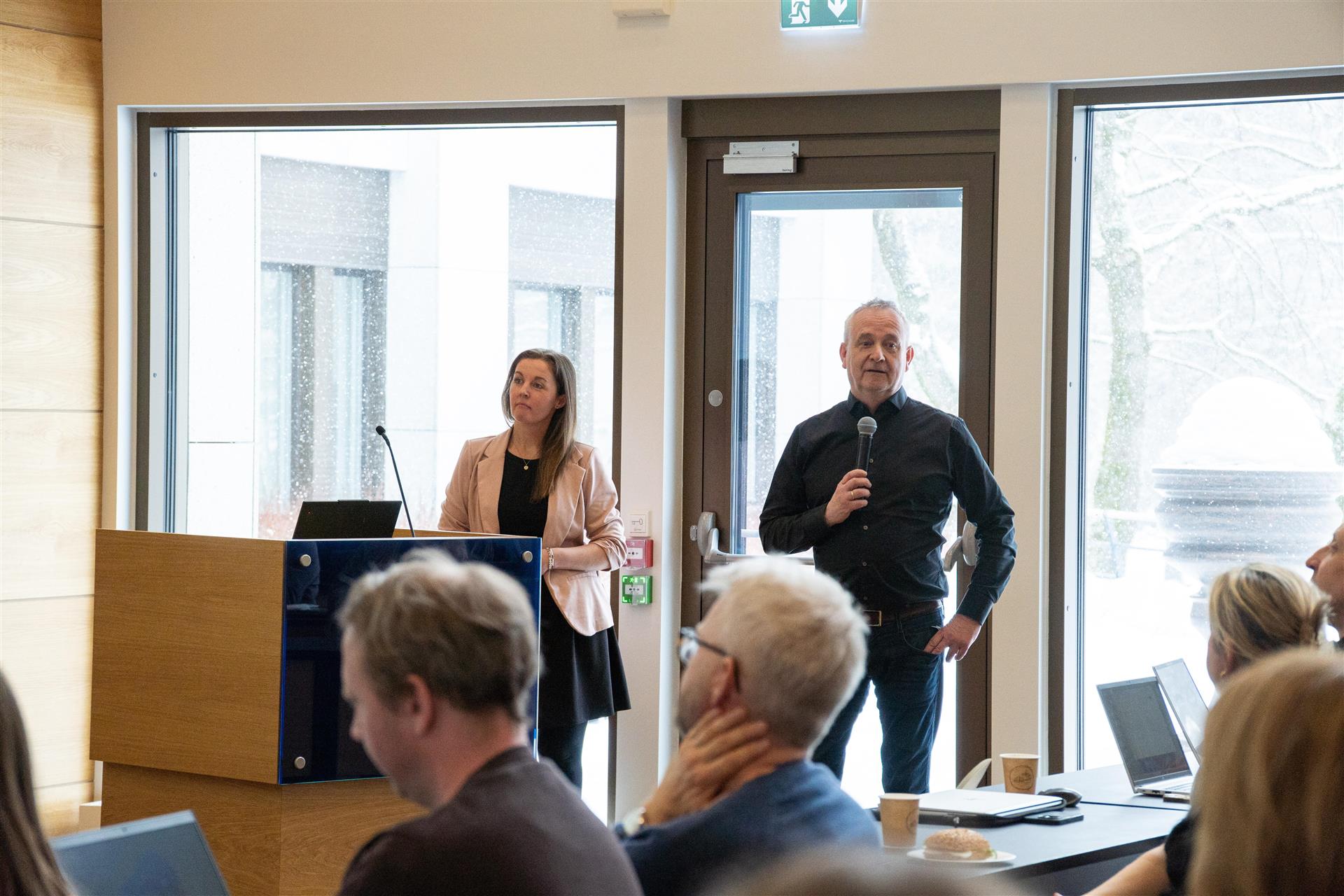 To representanter fra Aidn presenterer på et møte om innføring av elektronisk pasientjournal (EPJ). Deltakere sitter i salen og følger presentasjonen.